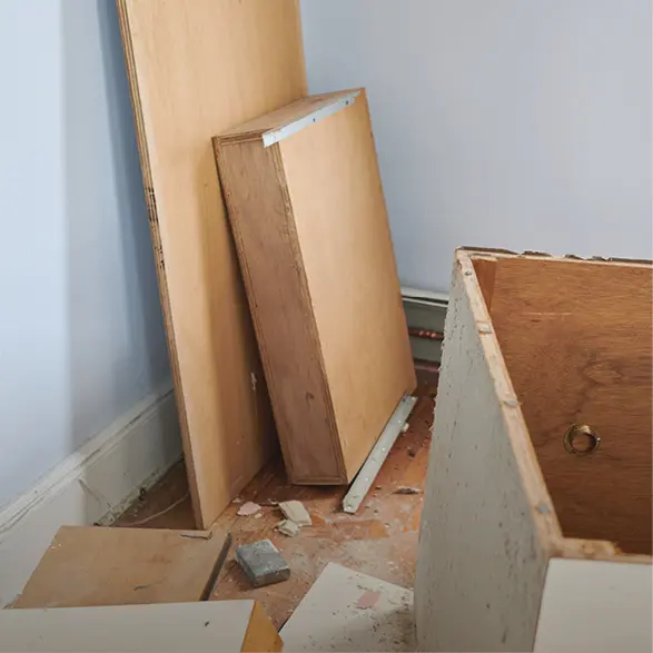 Alte Holzteile und ein ausgebauter Küchenschrank liegen auf dem Boden neben einer Wand während Renovierungsarbeiten